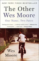 An African-American boy riding a bike looks back over his shoulder at the camera as he rides away down an empty street.