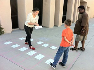 Two tutors and a student participating in a reading activity with note cards on the ground.