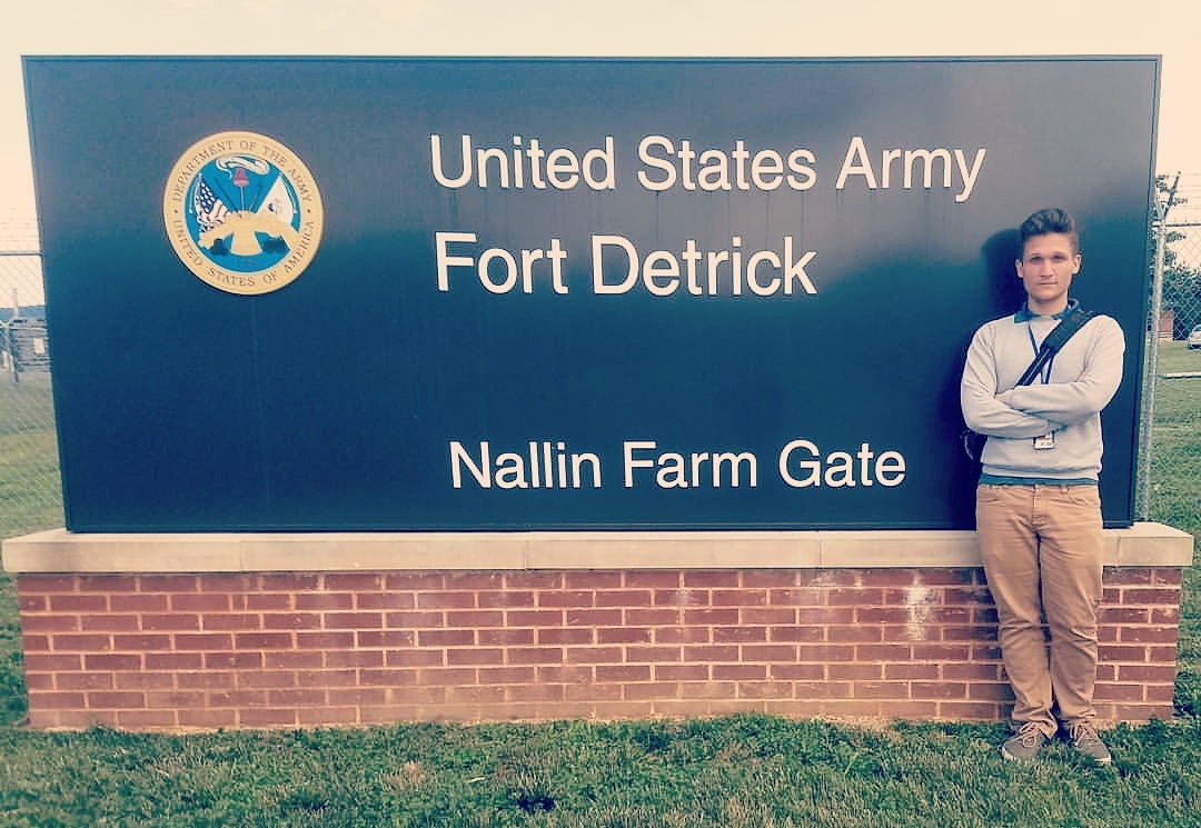 Federico looks calmly at camera while posing with U.S Army Base sign at Fort Detrick