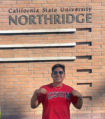 Smiling new CSUN student Marcus standing in front of CSUN sign