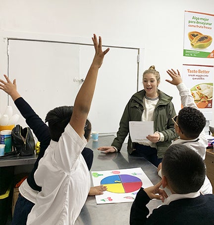 students raise their hands in a nutrition education class