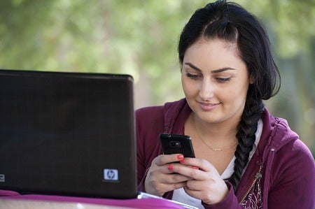A female student is using both her laptop and mobile device.