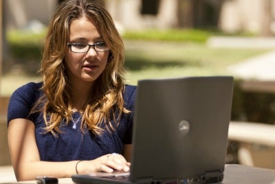 A photo showing a female CSUN student using her laptop outdoors.