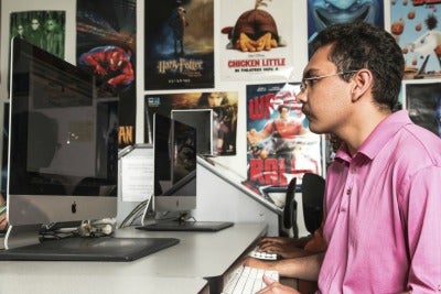 A photo showing a student working on a desktop computer with movie posters in the background.