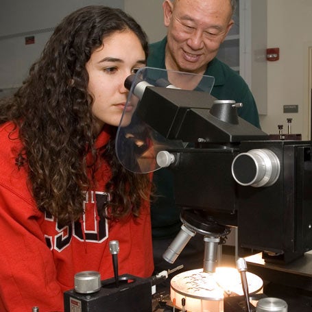 Student looking through a microscope while teacher watches.