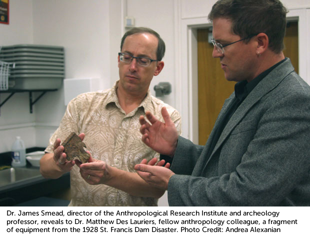 James Smead with caption: Dr. James Smead, director of the Anthropological Research Institute and archeology professor, reveals to Dr. Matthew Des Lauriers, fellow anthropology colleague, a fragment of equipment from the 1928 St. Francis Dam Disaster. Pho