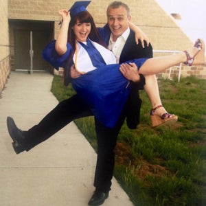 Kira Dimitri wearing a blue cap and gown being held up in the arms of her father