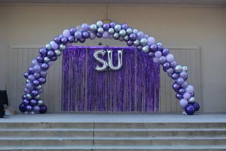 An arch of purple balloons, with the letters "SU" undernearth