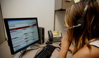 A woman at a computer using a headset microphone. 