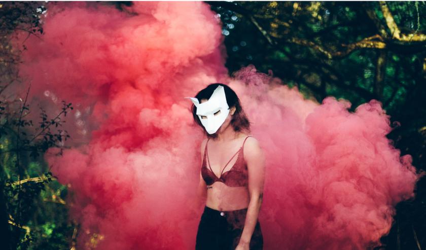 masked woman standing in front of a pink cloud of smoke