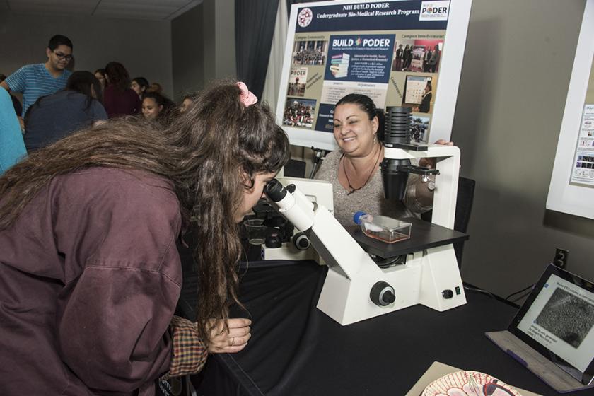 female student looks into microscope at the BUILD PODER table