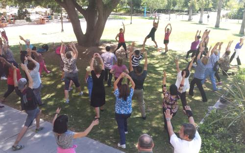 Large group of people with arms stretched high exercising outside