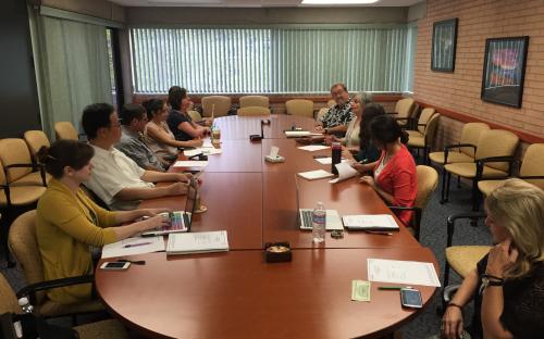 Group of people around a large wooden table having a meeting