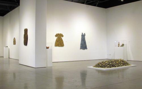  Install shot of back wall in the main room.  Two dresses made of costume jewelry.  Woman’s shoes covered in costume jewelry, beads, eggbeaters, string etc.