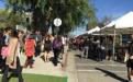 Crowd of people congregating in front of white farmers market tents