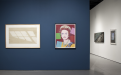 Image of Main Gallery back wall.  Two framed pop art images.  Image on left is a wood floor with window light shining.  Second image on right, is the Queen of England with brightly colored squares around her. 
