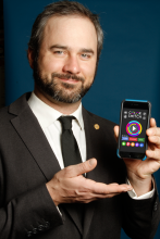 CSUN Alumni David Reichelt with a mobile phone showing his app, Color Switch