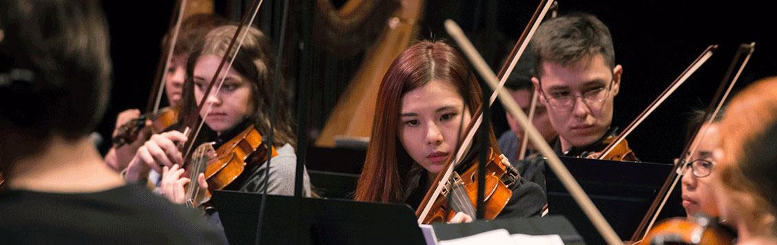 Female violinist intently playing within the orchestra.